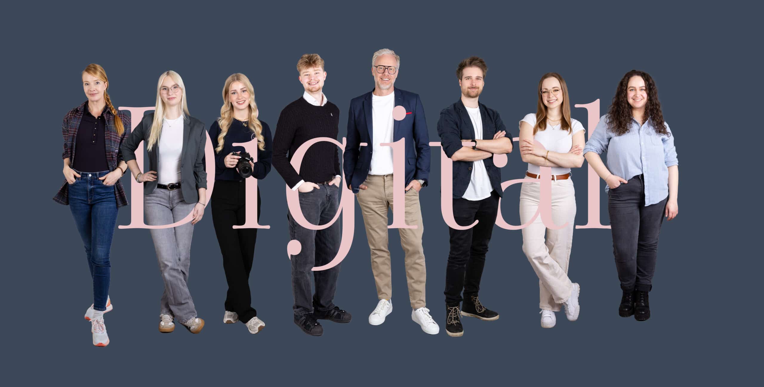 Eine gruppe von acht personen steht nebeneinander vor einem dunkelblauen hintergrund. Im vordergrund liegt der großflächige, halbtransparente schriftzug „digital“ in hellrosa, der die personen teilweise überschneidet. Die gruppe ist gemischt gekleidet, von legeren jeans und t shirts bis hin zu sakkos und blusen. Eine person hält eine kamera in der hand. Alle blicken lächelnd in die kamera.